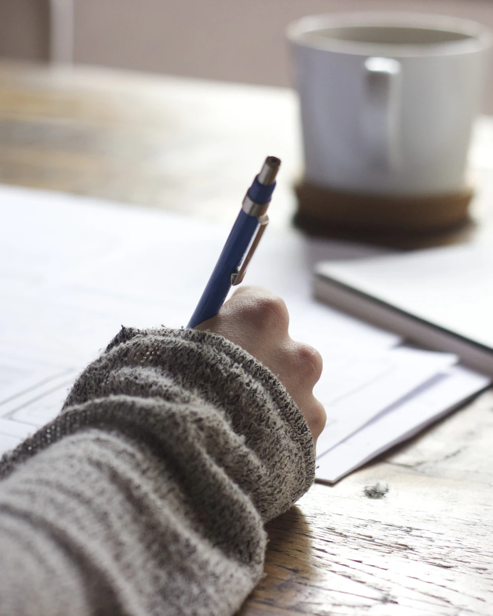 Mano escribiendo en un cuaderno junto a una taza